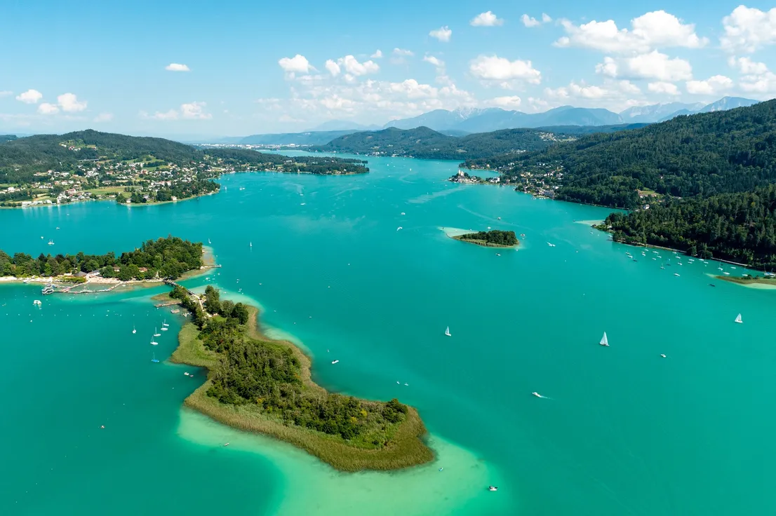Luftaufnahme vom türkisfarbenen Wörthersee mit Segelbooten und bewaldetem Ufer